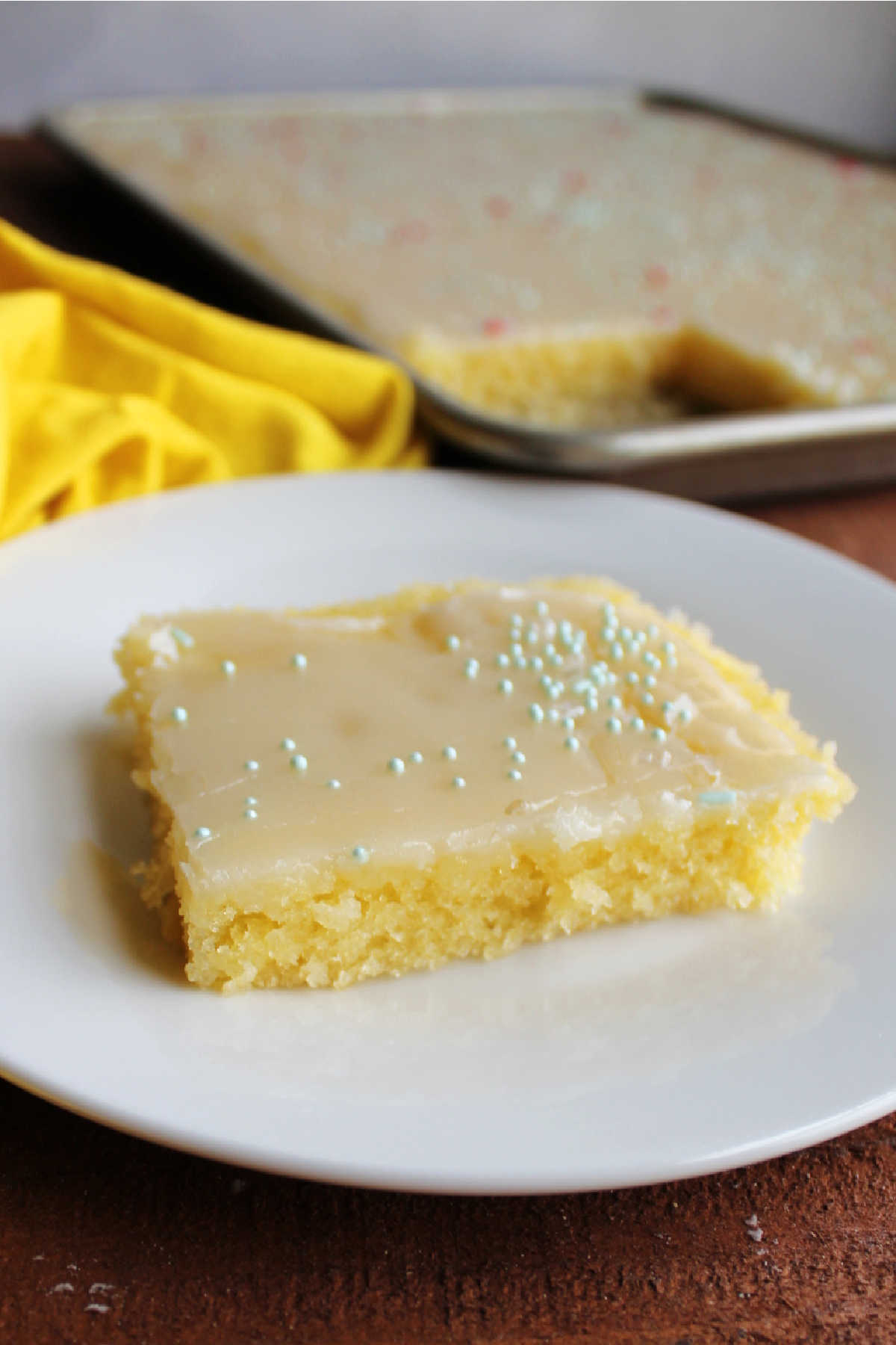 Piece of lemon Texas sheet cake with glossy icing and spinkles on top.