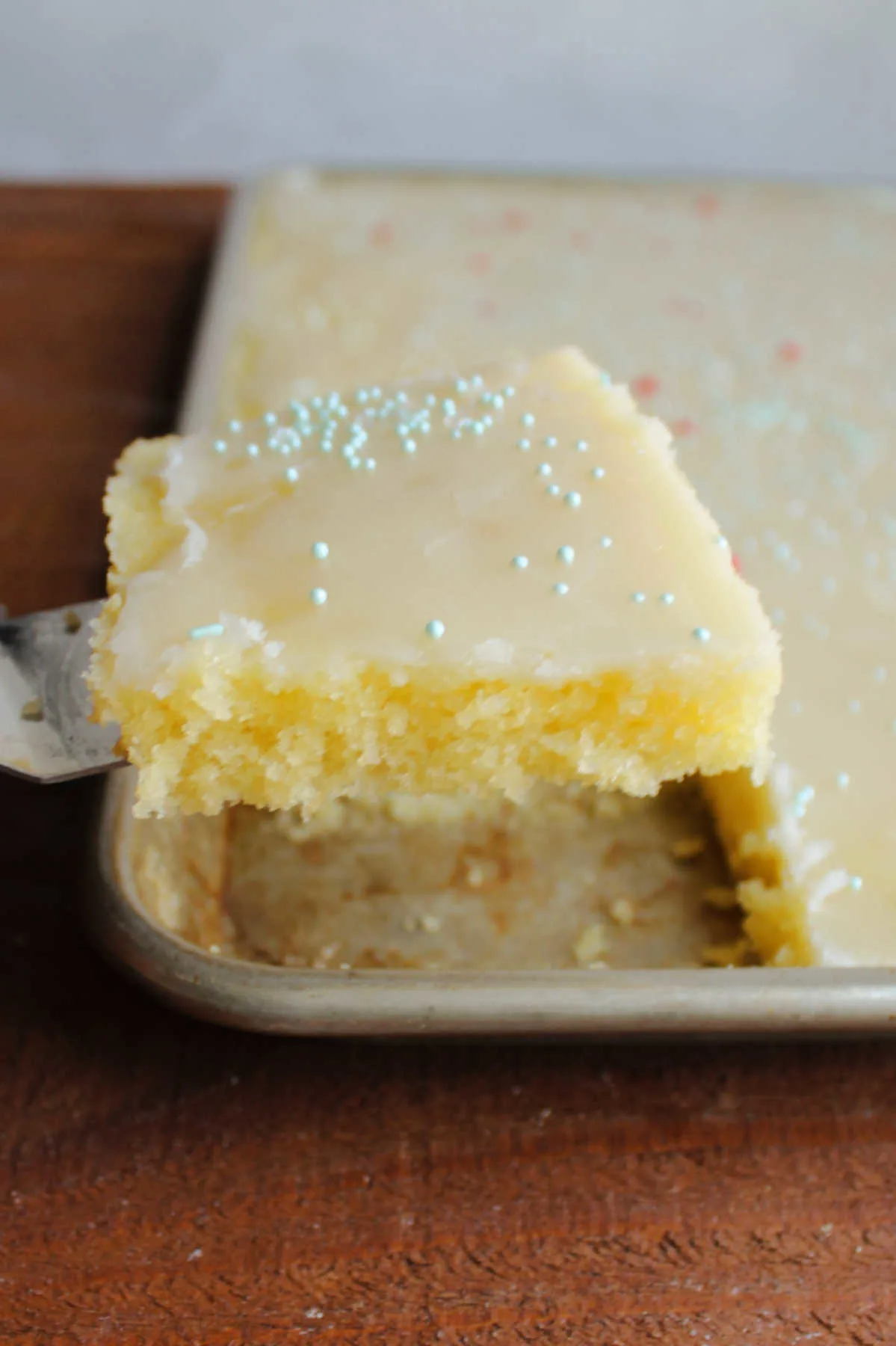 Lifting first slice of lemon Texas sheet cake out of pan showing soft texture.