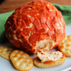 Cheeseball coated in chopped pepperoni next to crackers.