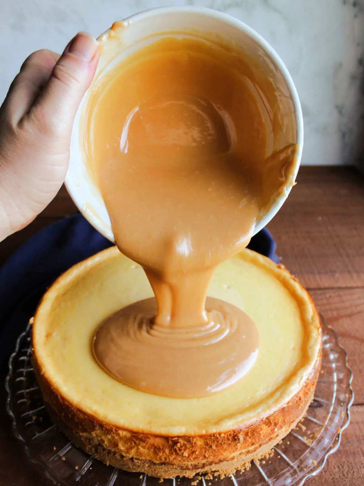 Pouring warm caramel sauce over cooled cheesecake.