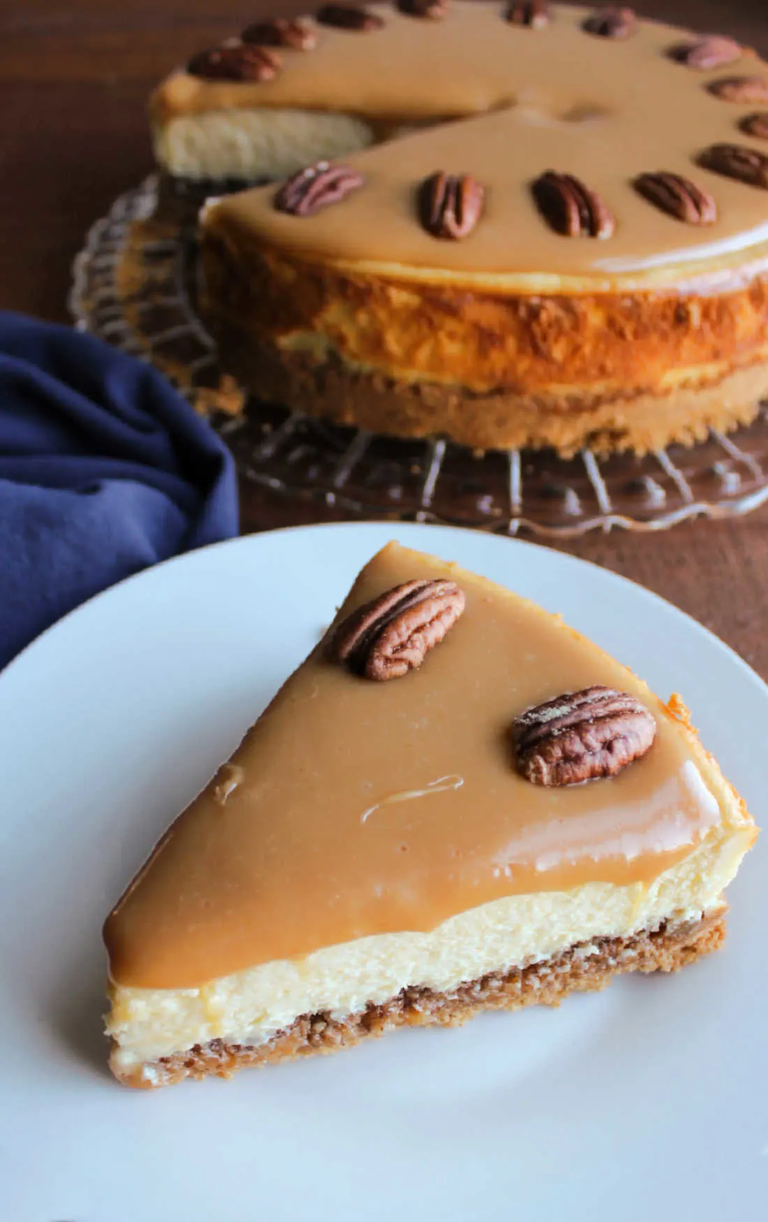 Looking down on a slice of cheesecake with a smooth caramel layer and pecans on top.