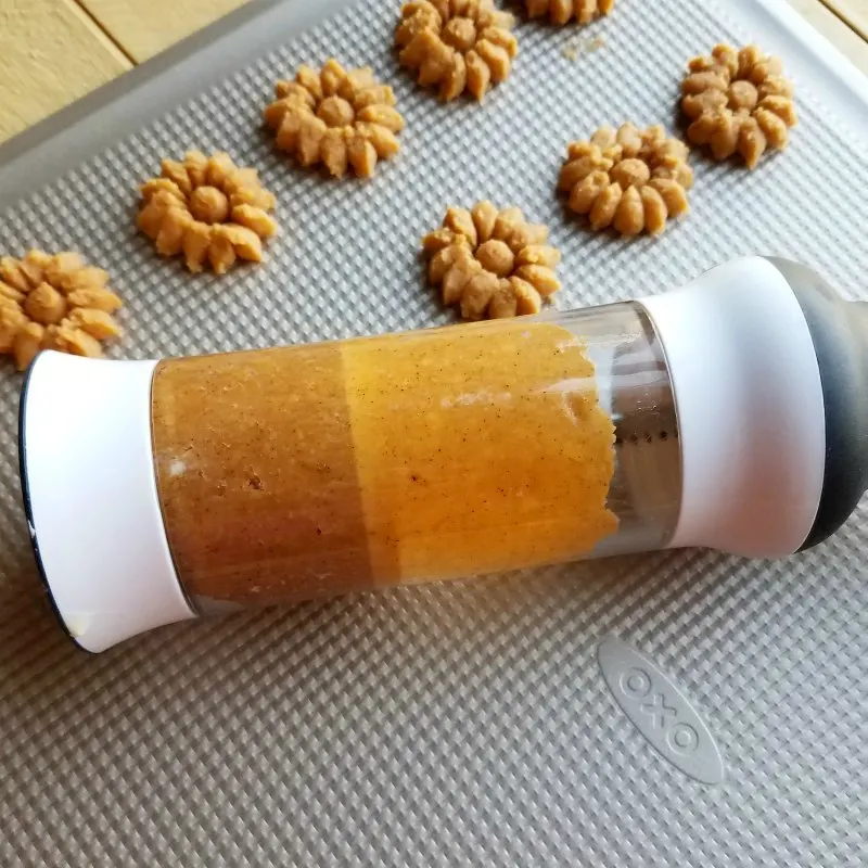 cookie press filled with cracker dough and some crackers pressed out onto cookie sheet.