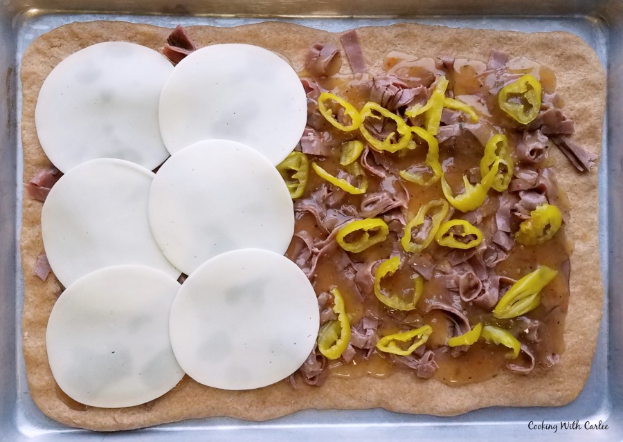assembling a pizza, one side with slices of provolone on it, the other showing the meat and peppers