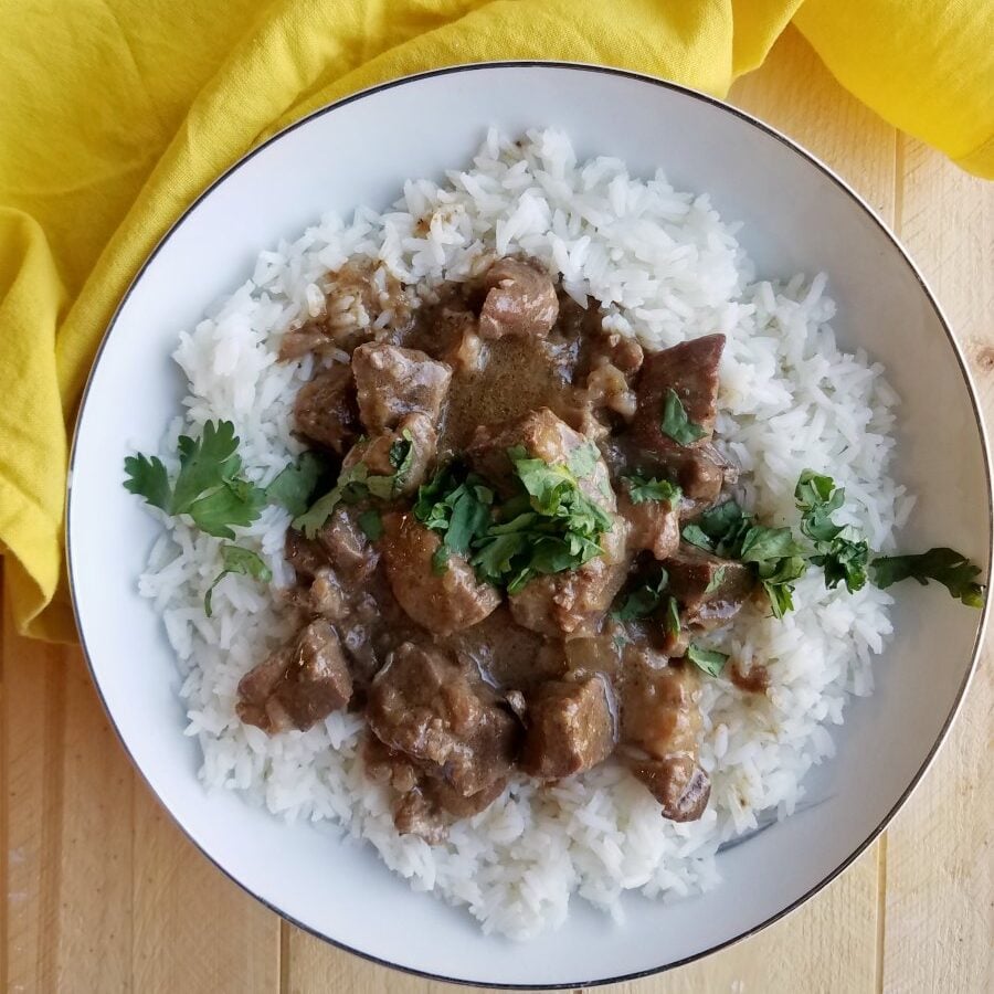 Bowl of rice topped with curried lamb stew and fresh herbs.