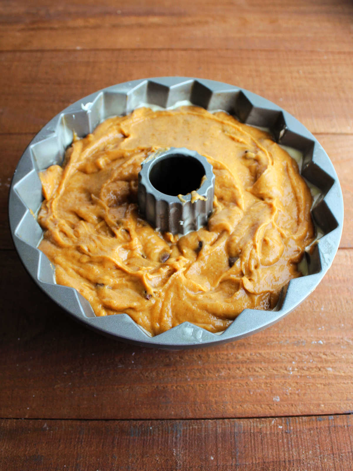 Remaining pumpkin cake batter smoothed over cream cheese filling in bundt cake pan, ready to go in the oven.