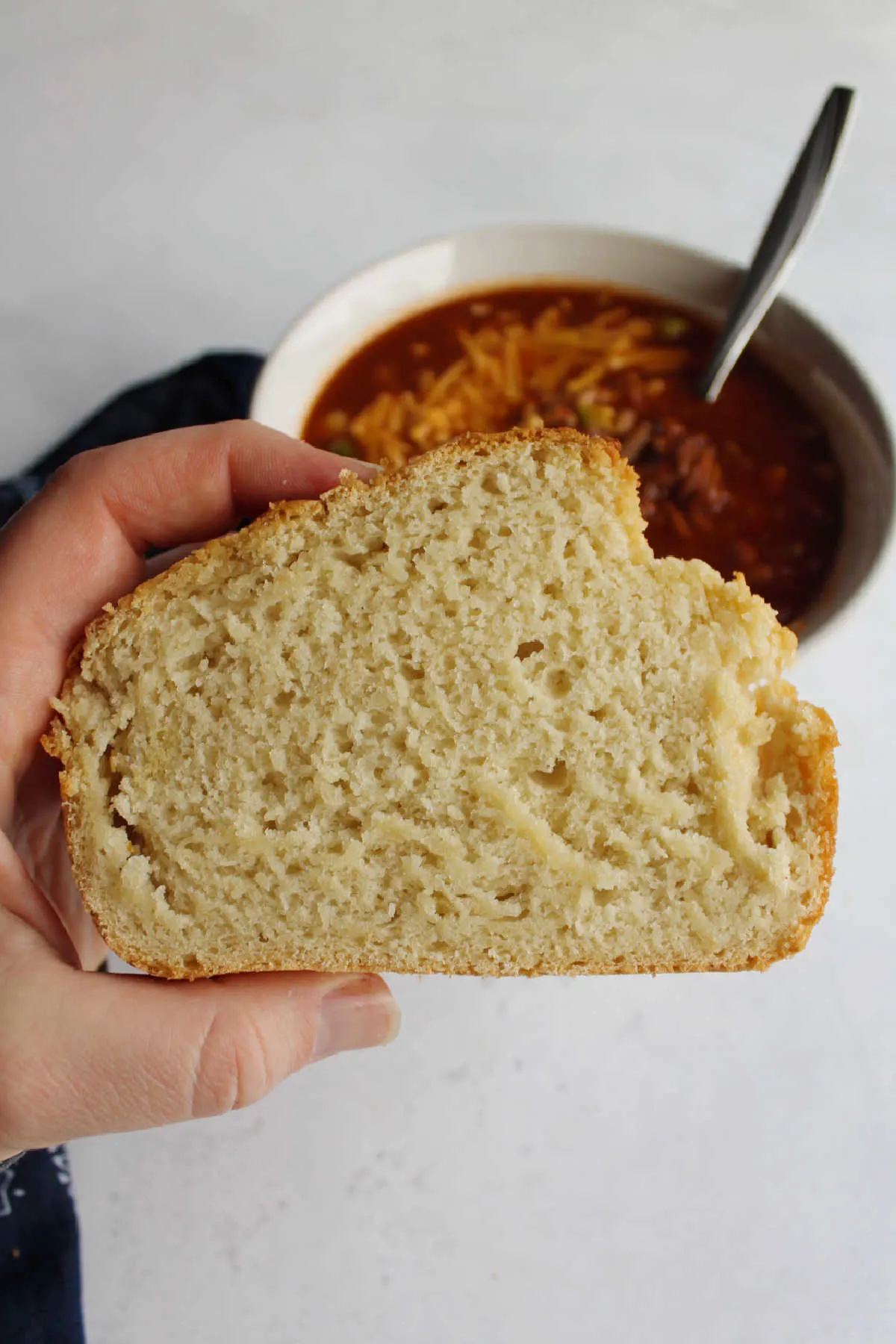 Hand holding slice of beer bread in front of pulled pork chili.