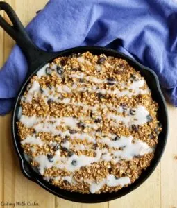 cast iron skillet filled with baked oatmeal drizzled with glaze.