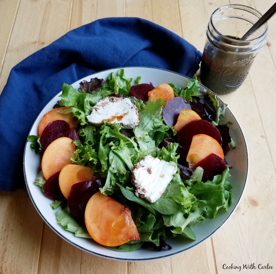 greens topped with sliced beets, persimmons and goat cheese with jar of dressing