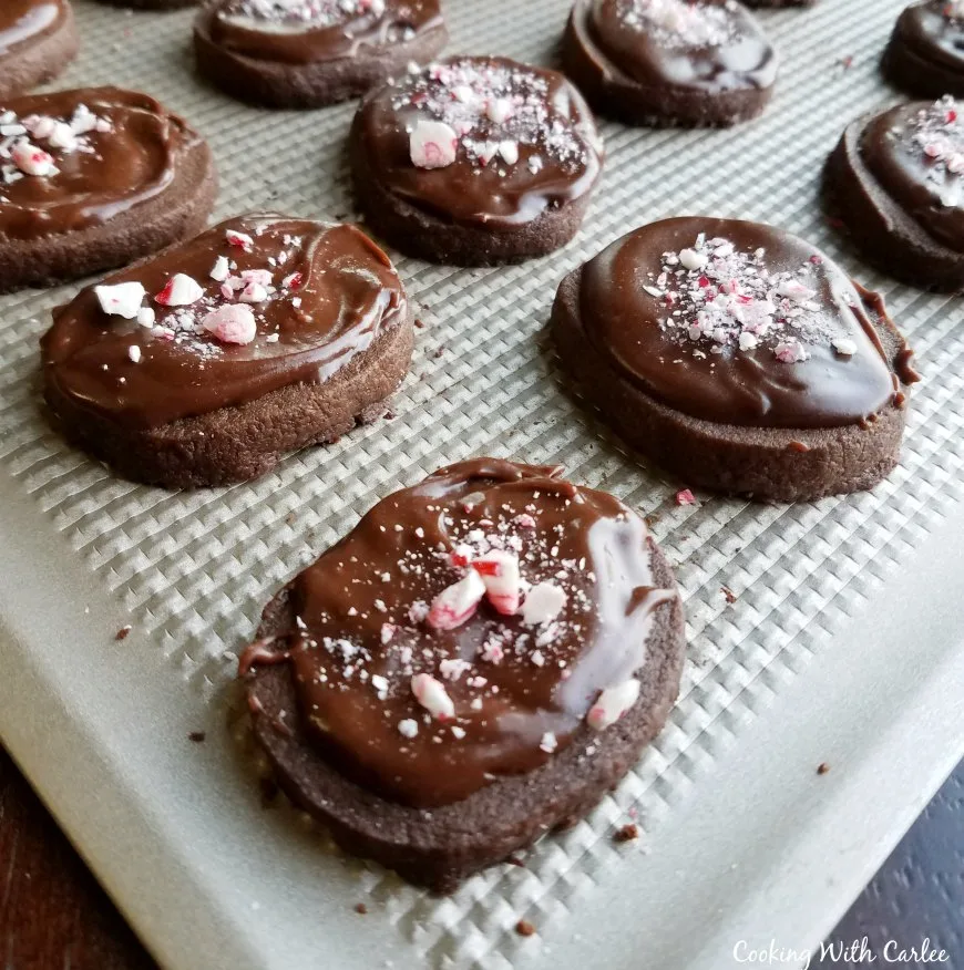 mocha shortbread cookies with chocolate frosting and bits of candy canes on cookie sheet.