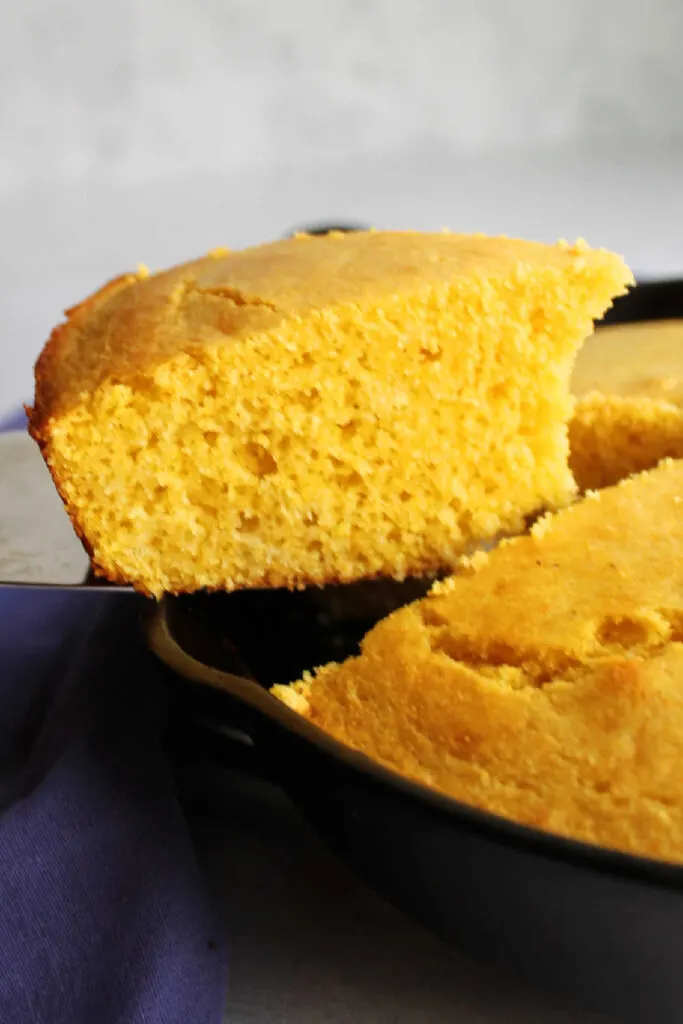 Lifting slice of soft yellow cornbread out of cast iron skillet.
