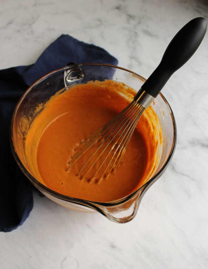 Mixing bowl filled with maple pumpkin pie filling and whisk.
