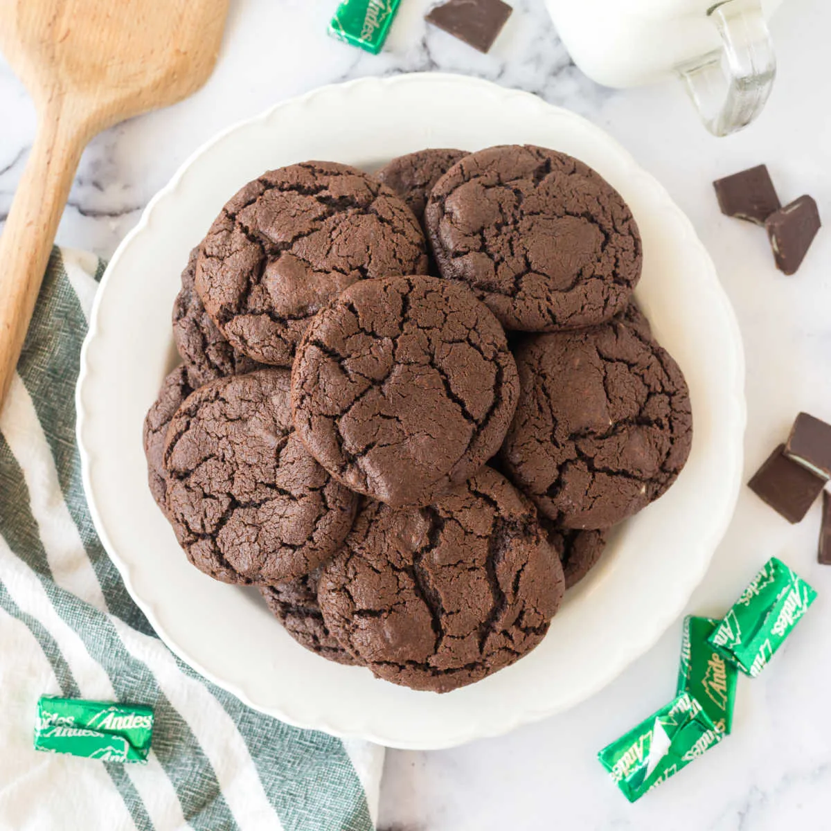 White plate piled high with chocolate mint cookies showing crackly exterior surrounded by Andes mints candies.