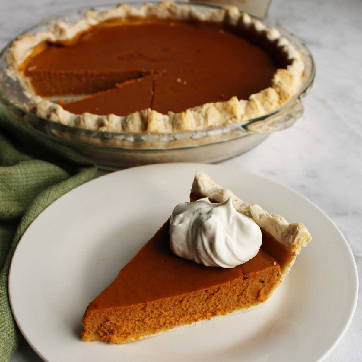 Slice of maple pumpkin pie topped with maple whipped cream in front of remaining pie.