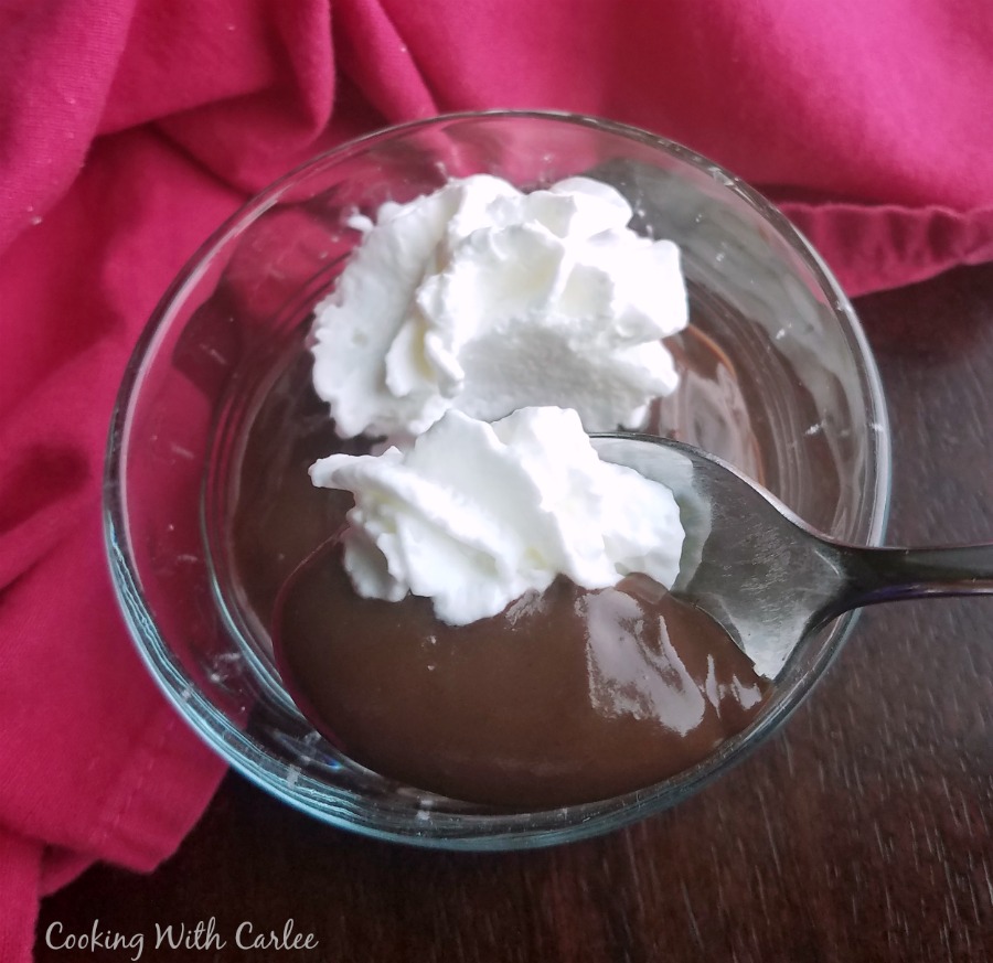 small bowl of chocolate pudding with whipped cream on top, spoon taking first bite.