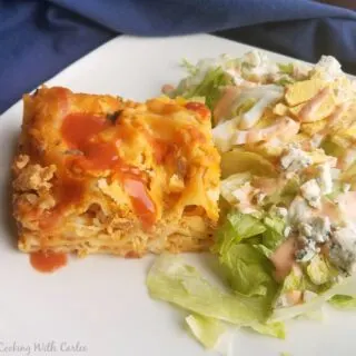 slice of creamy buffalo chicken lasagna on plate with blue cheese topped salad.