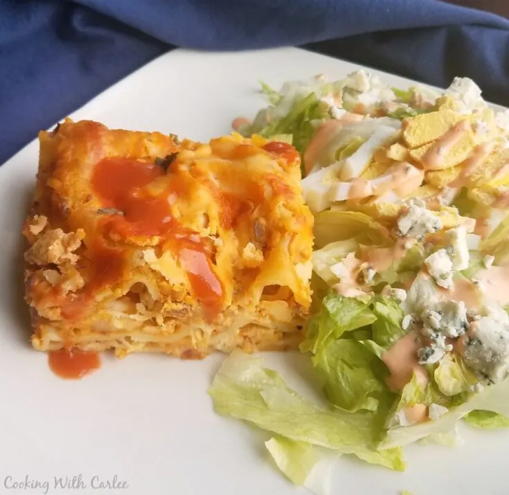 slice of creamy buffalo chicken lasagna on plate with blue cheese topped salad.