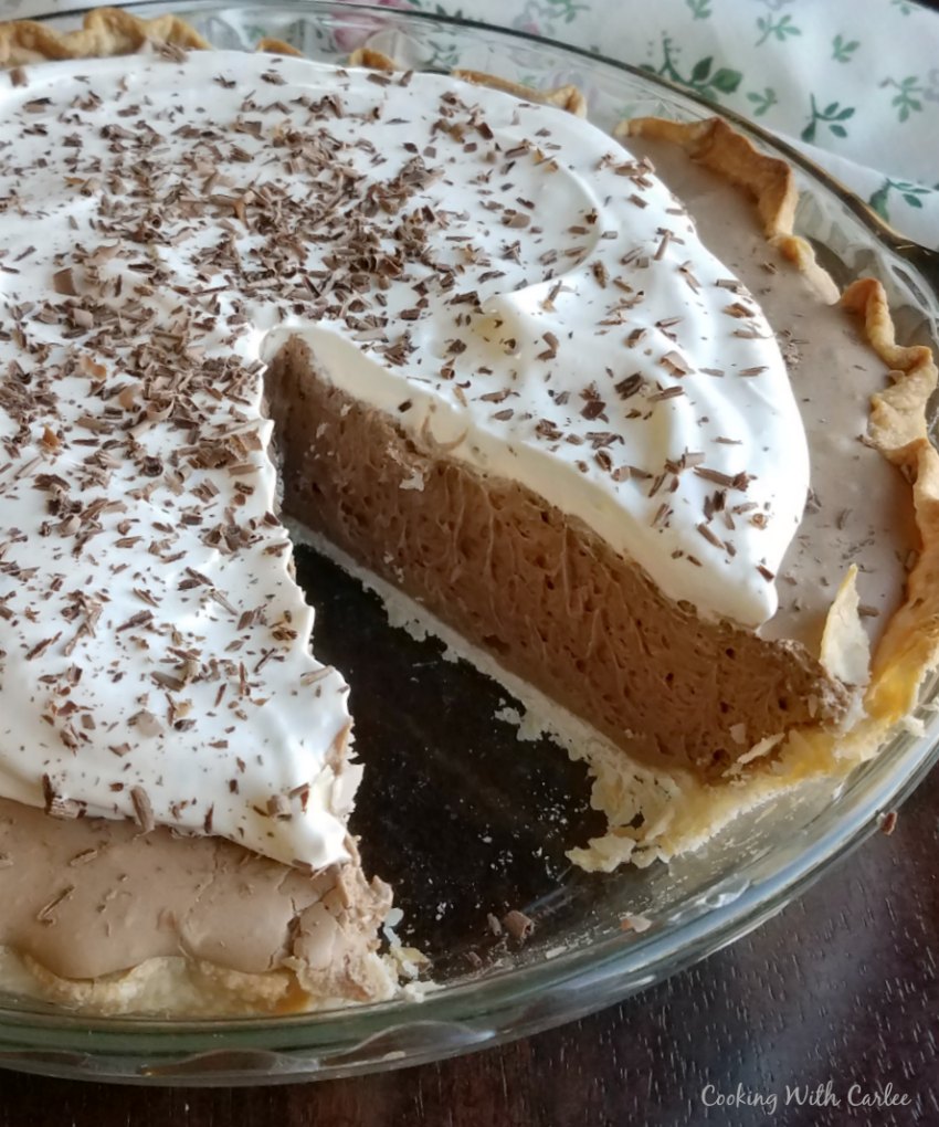 Chocolate french silk pie with whipped cream and chocolate shavings on top, one slice missing.