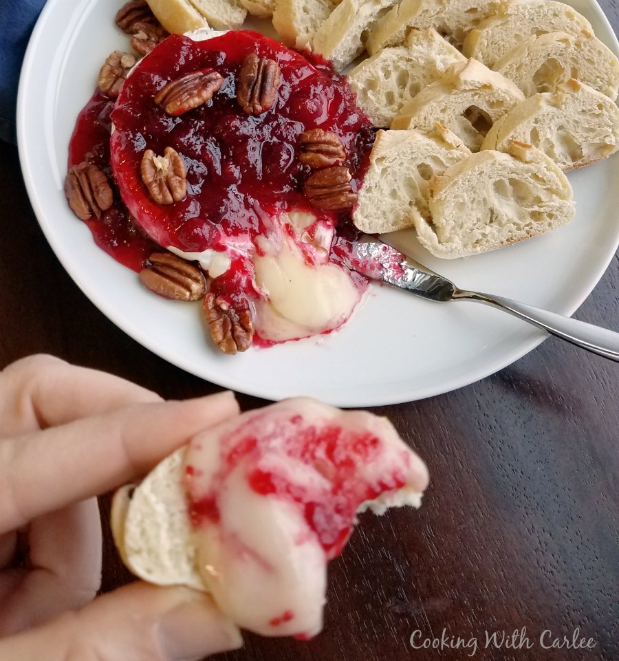 plate of gooey brie baked with cranberry maple sauce and spread on a baguette slice.