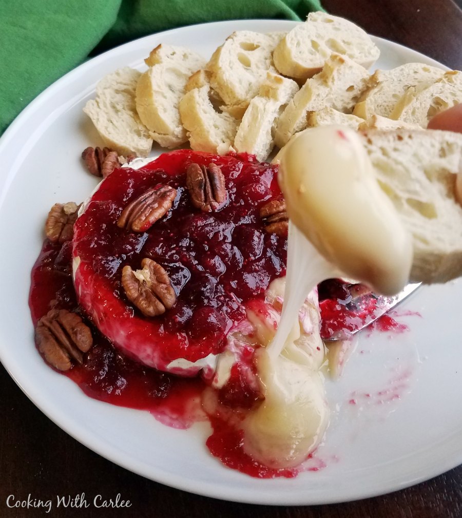 plate of baked brie with cranberry sauce and pecans with baguette slice dipped in gooey cheese.