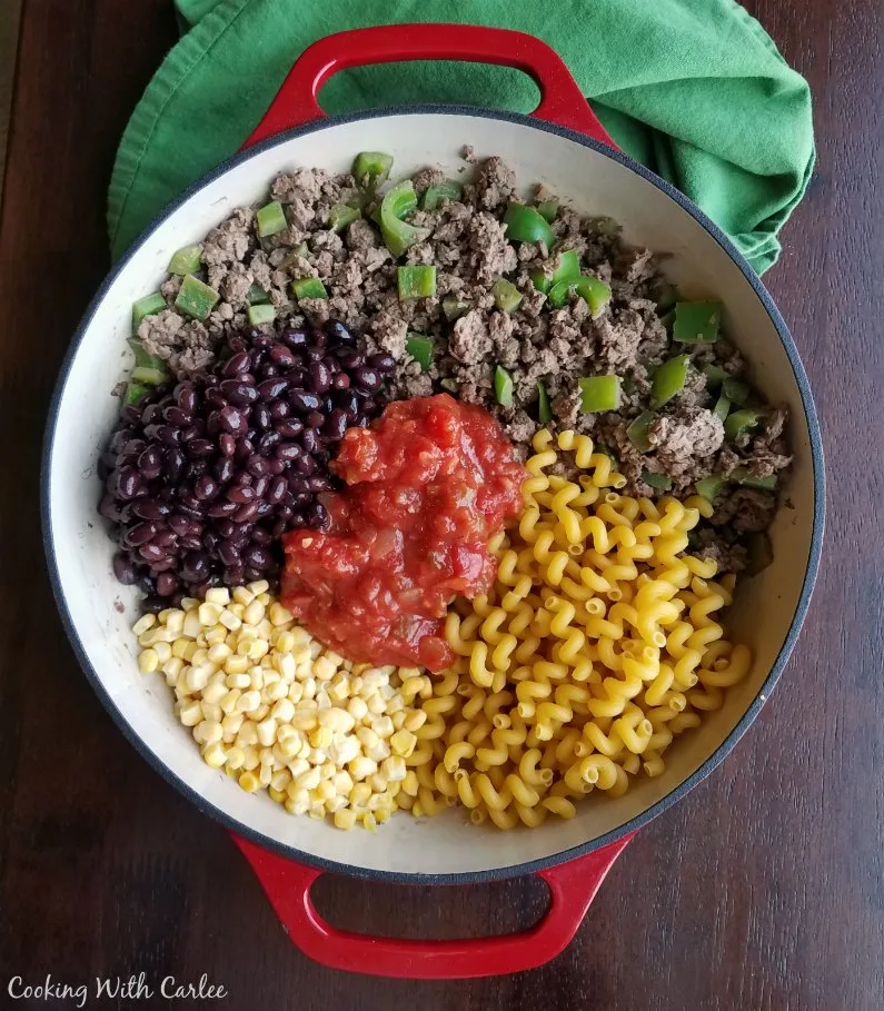 Ingredients including ground beef, peppers, black beans, corn, salsa, and pasta in pan ready to be cooked. 