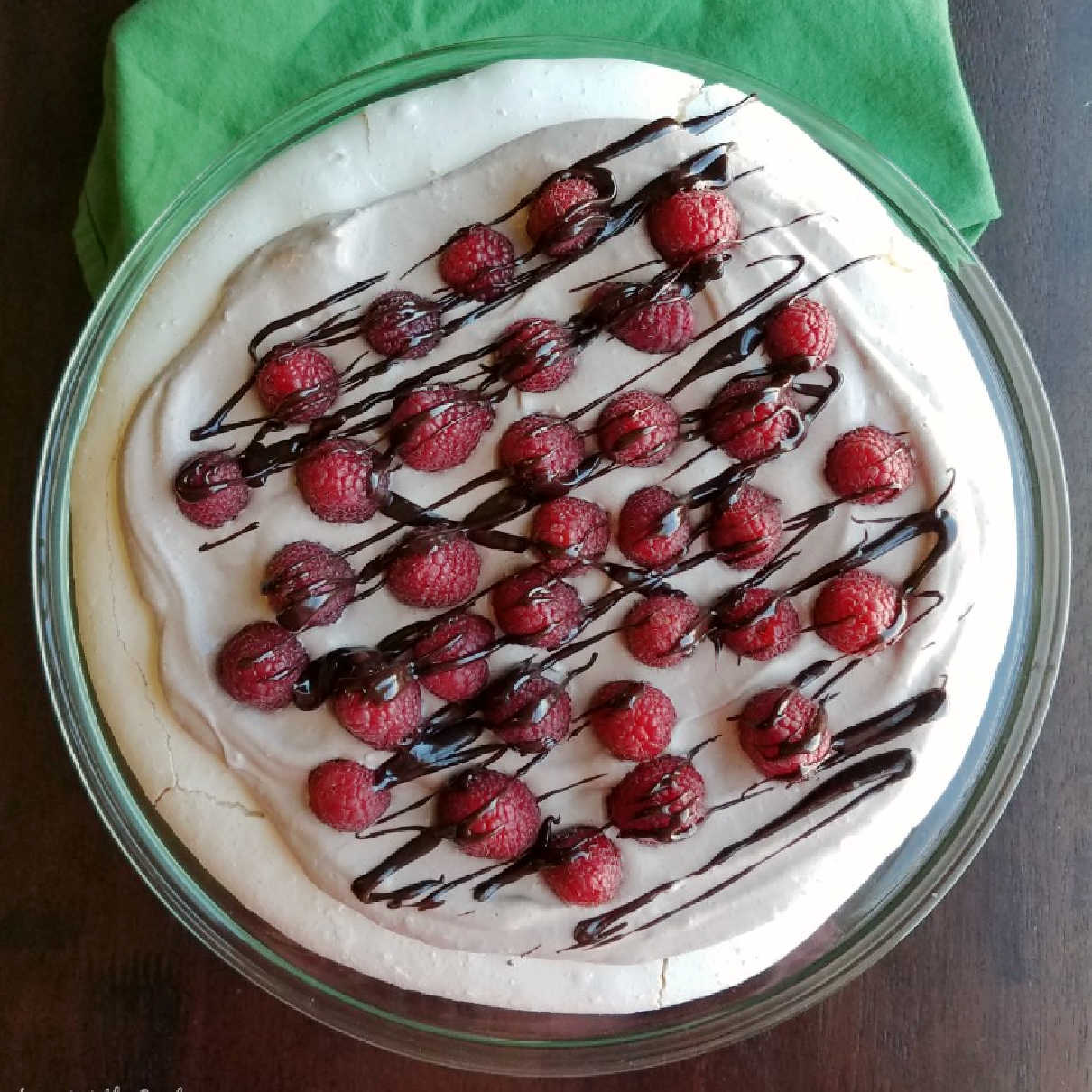 looking down on white pavlova with chocolate whipped cream, raspberries and drizzle of chocolate on top.