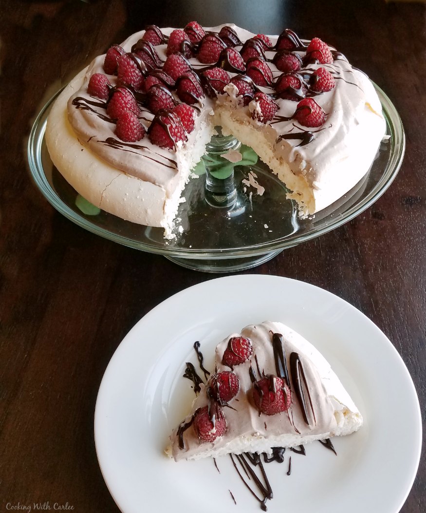 first slice of chocolate raspberry pavlova served with remainder on glass cake plate in background.