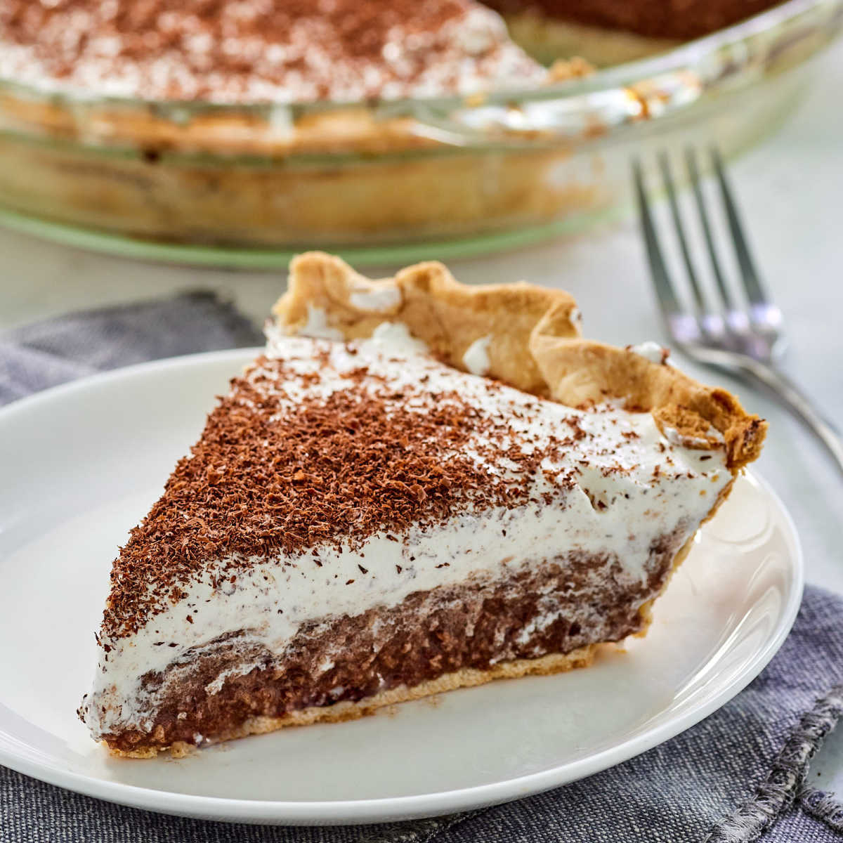 Piece of homemade french silk pie with rich chocolate filling that is more solid than a pudding filling topped with whipped cream and chocolate shavings, ready to eat.