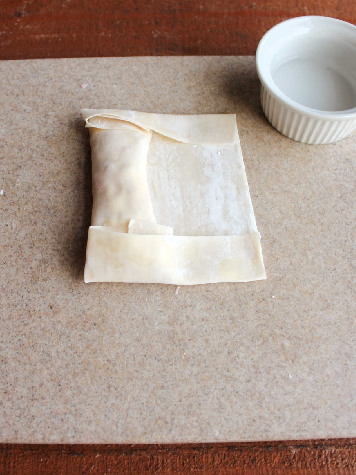 Folding the ends of the egg roll wrapper down around filling.