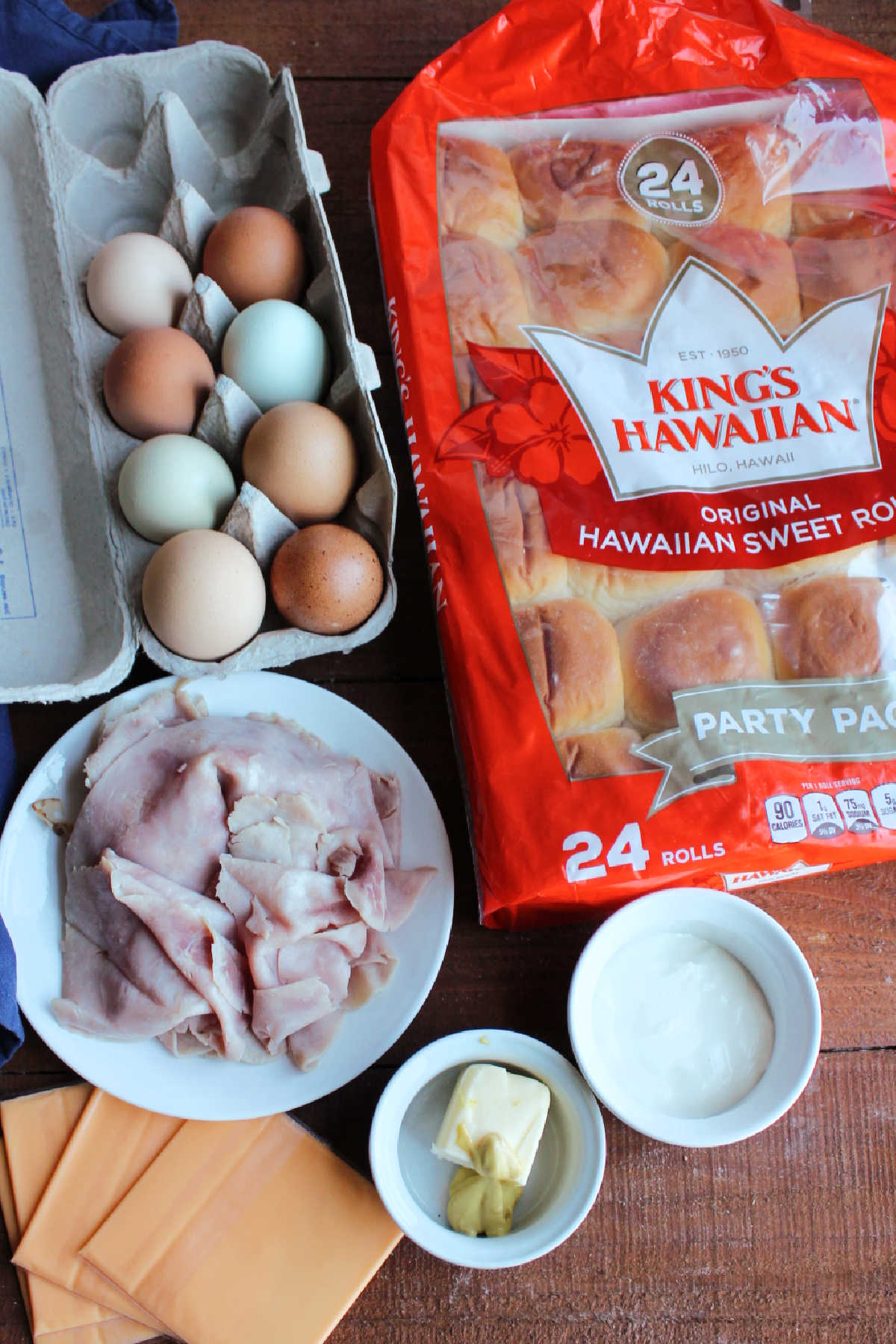 Ingredients for breakfast sliders including eggs, ham, cheese, dinner rolls, sour cream, butter and dijon mustard. 