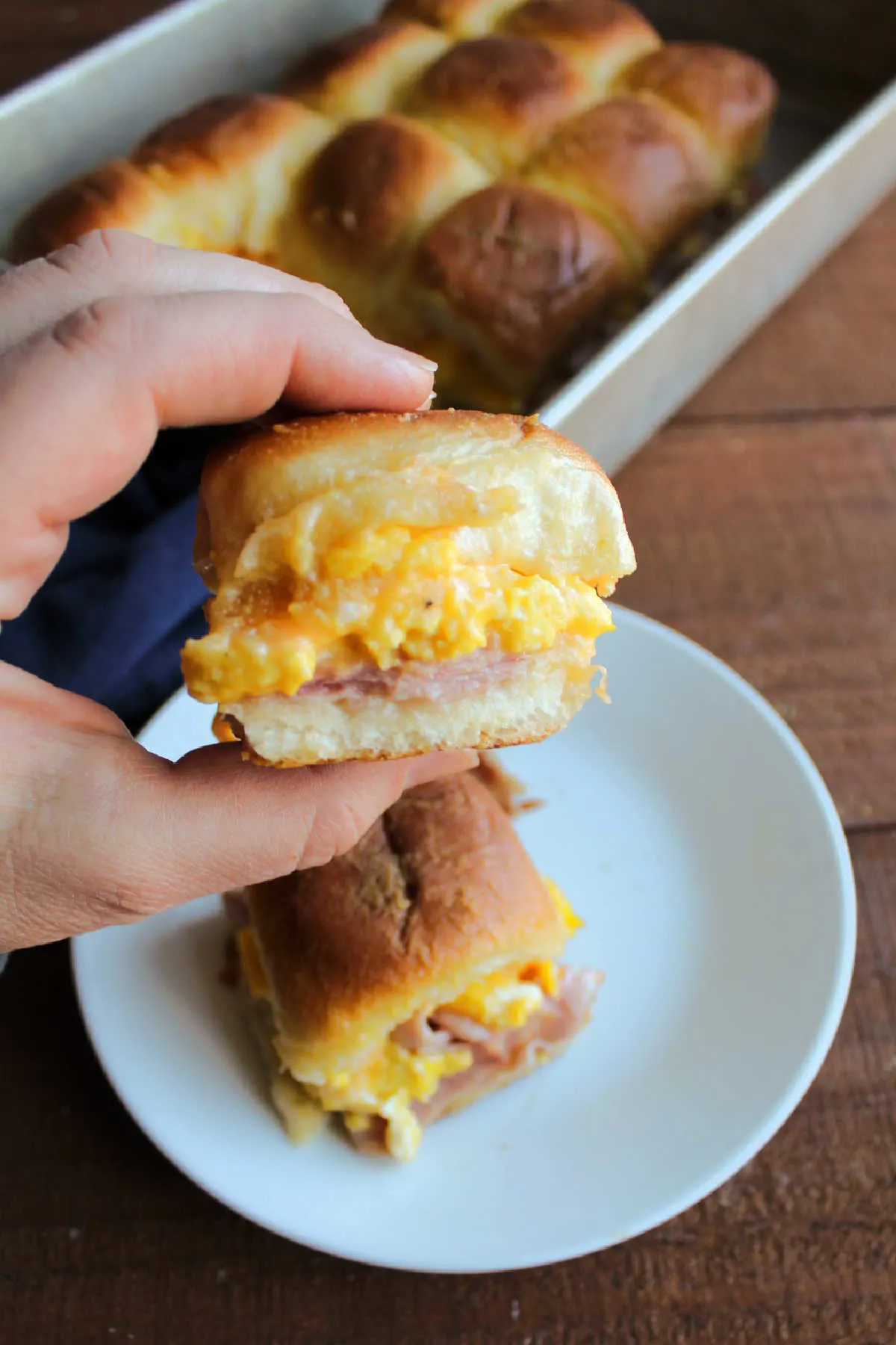 Hand holding freshly baked ham, egg and cheese slider, ready to heat.