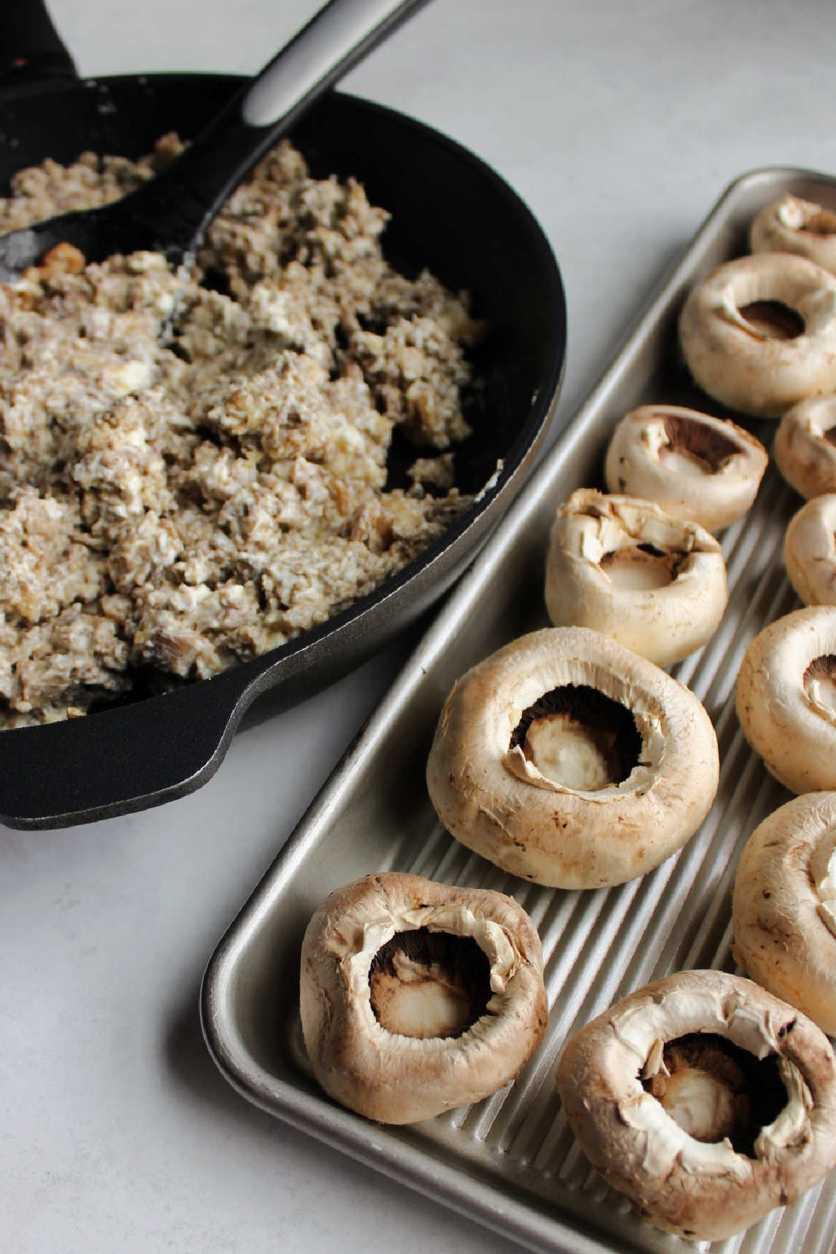 Tray of mushroom tops next to skillet filled with cream cheese and sausage mixture.