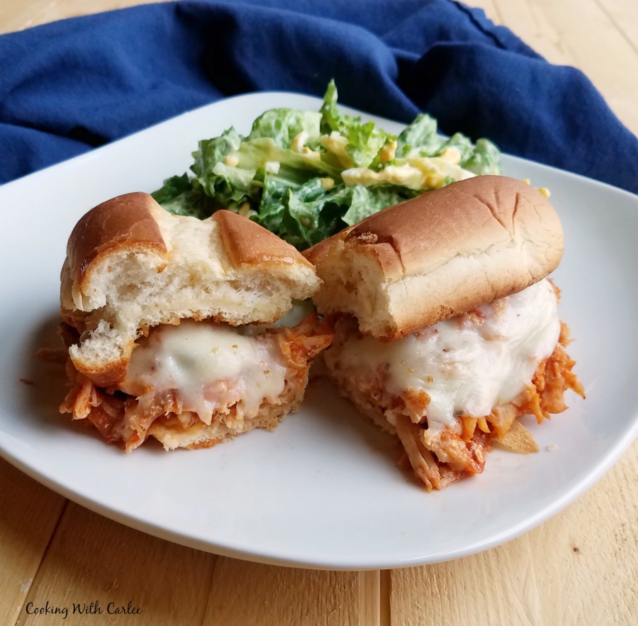 Shredded chicken sandwich with tomato sauce and melted cheese served with salad.