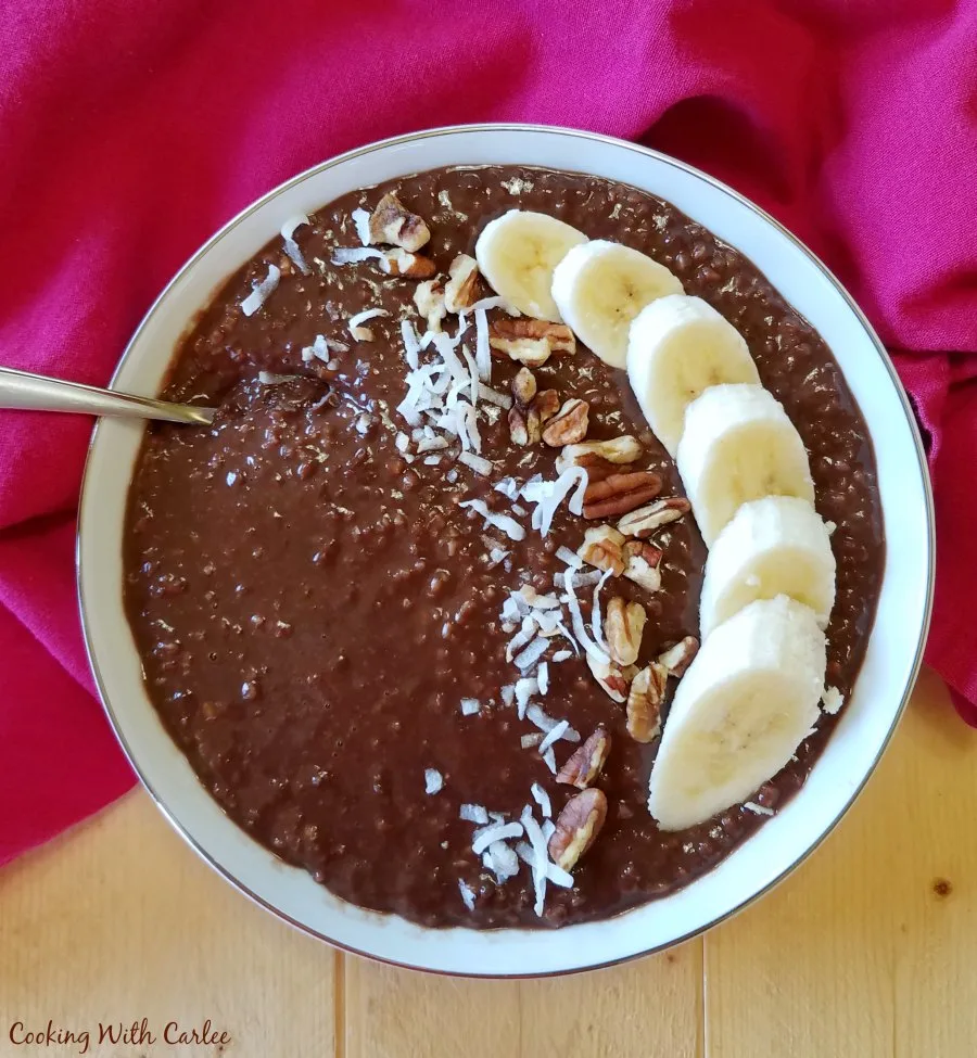 bowl of chocolate oatmeal topped with sliced bananas, coconut and pecans.