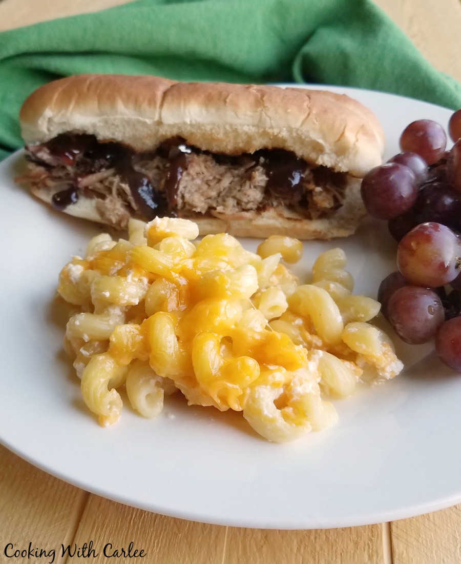 plate of mac and cheese with grapes and pulled pork sandwich.