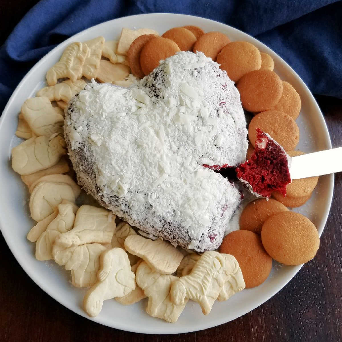 serving plate with heart shaped red velvet cheese ball coated in white chocolate shavings with vanilla wafers and animal crackers for eating.