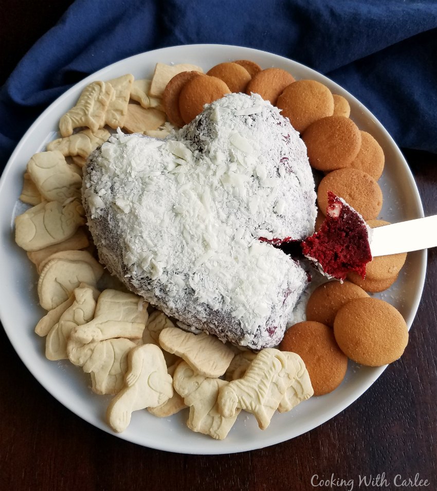 serving plate with heart shaped red velvet cheese ball coated in white chocolate shavings with nilla wafers and animal crackers for eating