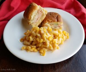 plate with pile of slow cooker macaroni and cheese with corn and hot ham and cheese sliders.