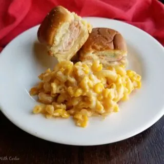 plate with pile of slow cooker macaroni and cheese with corn and hot ham and cheese sliders.