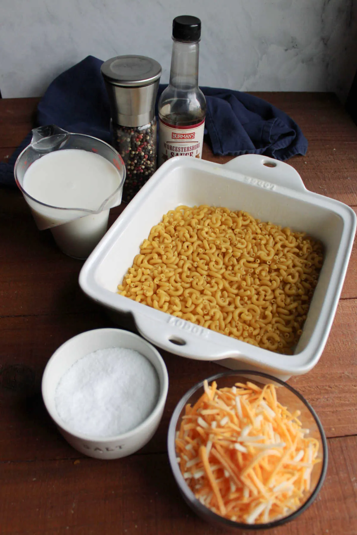 Ingredients including pasta, cheese, milk, salt, pepper, and worcestershire sauce ready to be baked into macaroni and cheese.