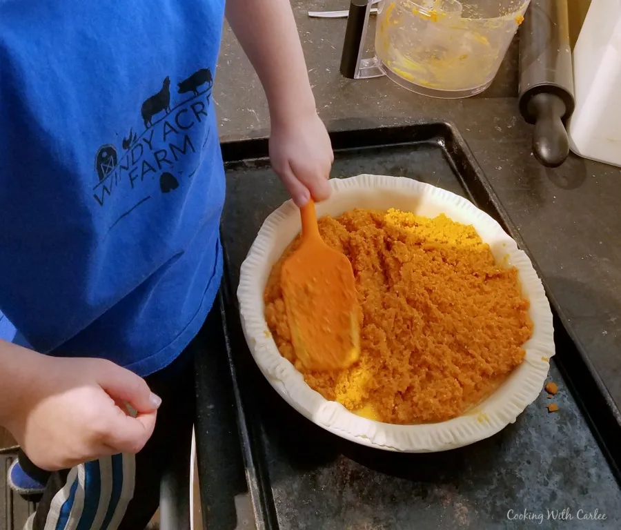 kid spreading mashed carrot filling into prepared pie crust.