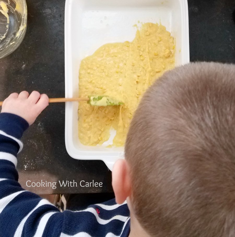 kid spreading cornmeal mixture in casserole dish.