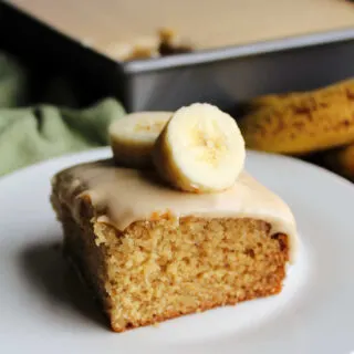 Square piece of banana cake topped with brown sugar icing and a couple of banana slices, ready to eat.