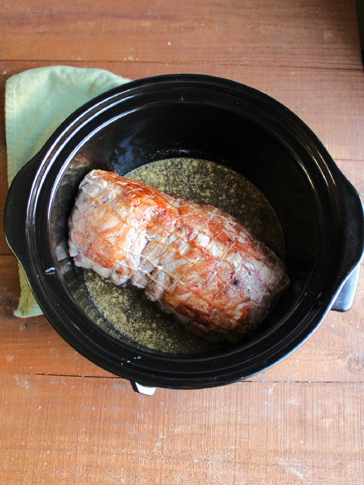 Crockpot with browned pork roast and sauce ingredients, ready to cook.