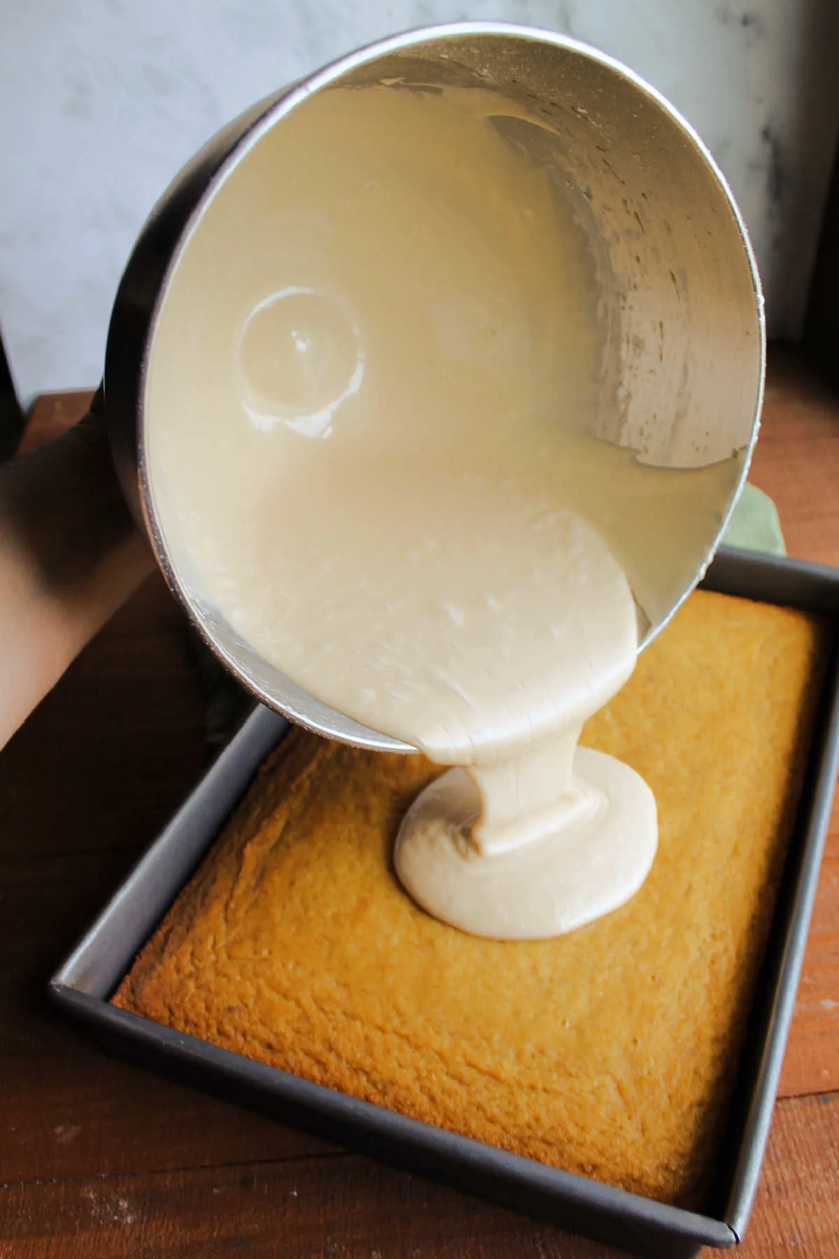 Pouring warm brown sugar icing over cold banana cake.