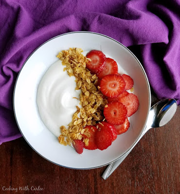 bowl of yogurt topped with strawberry slices and golden honey coconut granola