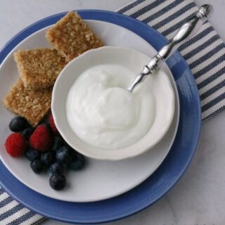 Bowl of vanilla yogurt next to three squares of brown sugar oat bars and fresh berries.