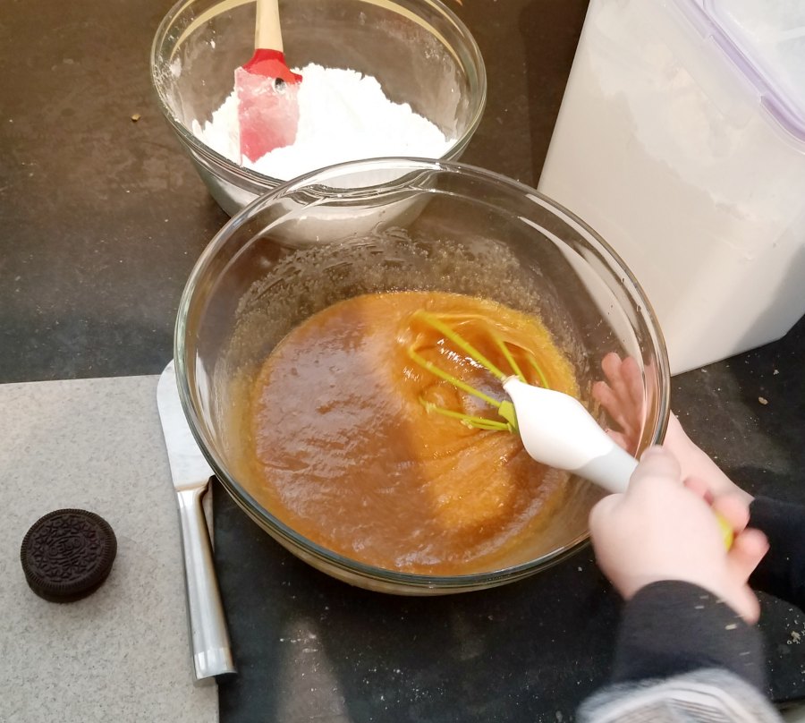 kid's hand stirring bowl of blondie batter with whisk.