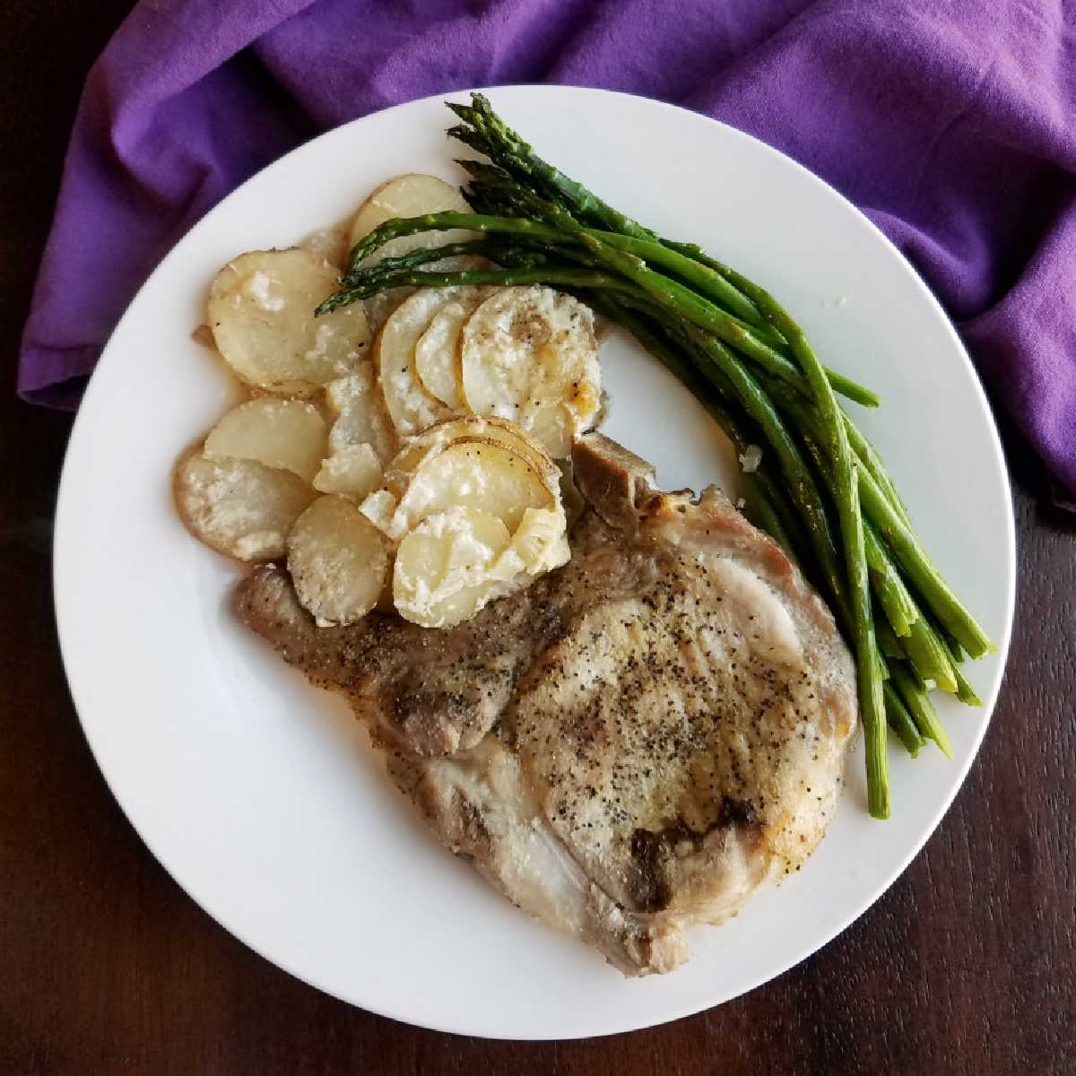 Dinner plate with scalloped potatoes, a pork chop and asparagus ready to eat.
