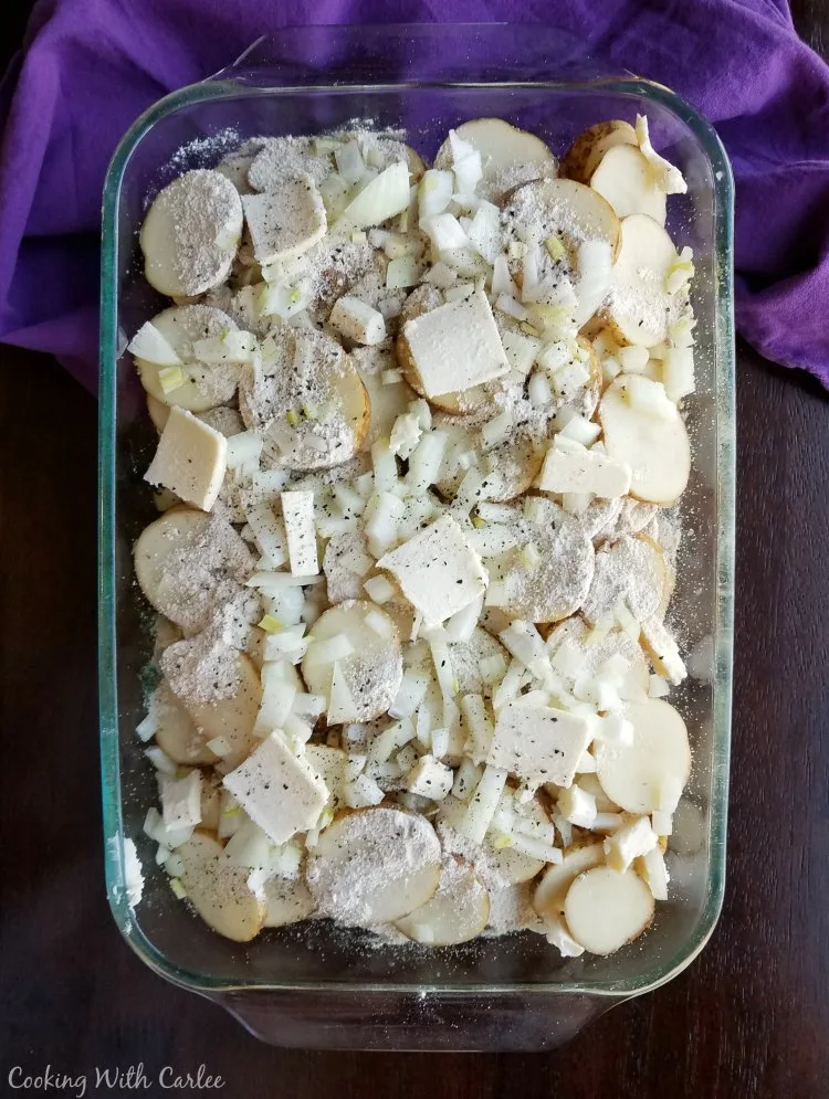 glass casserole dish filled with sliced potatoes, butter and onions.