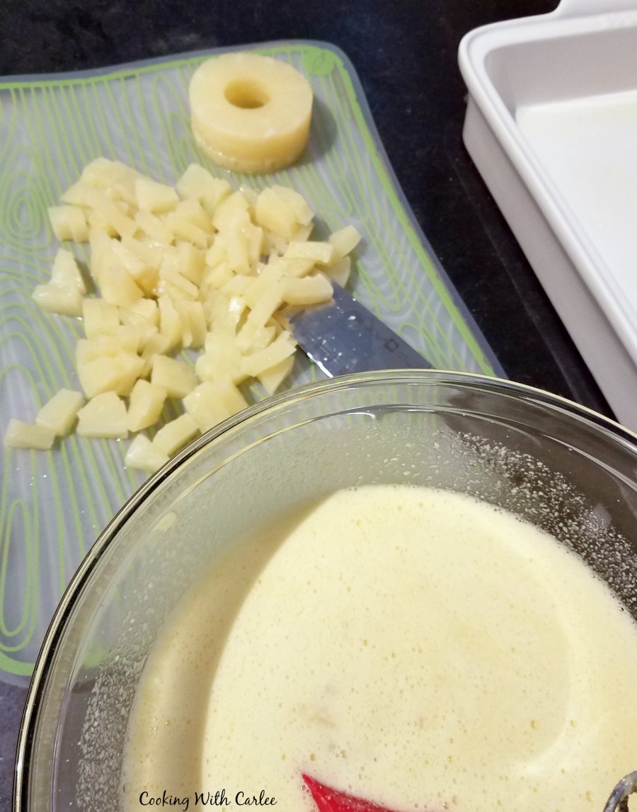 pineapple getting chopped on cutting board next to mixing bowl of egg milk mixture.